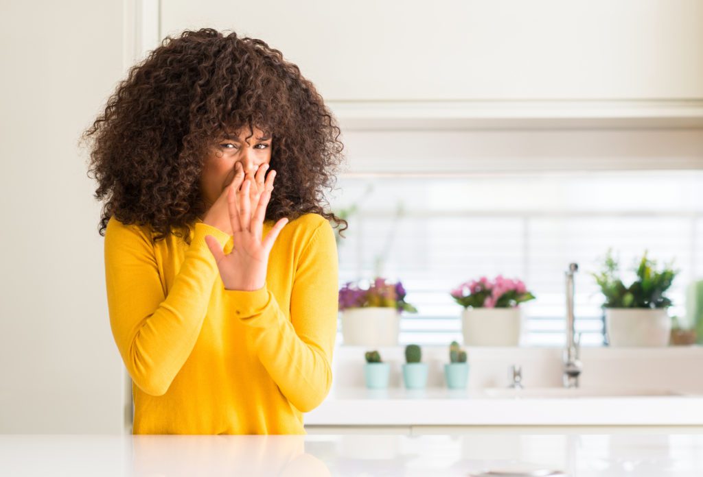 woman reacting to odor due to mold in kitchen cabinets